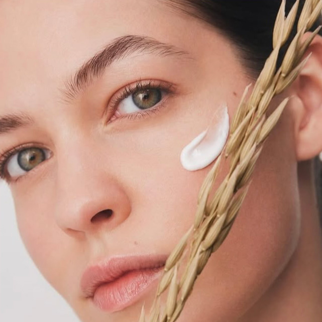 Frau mit Cremefleck auf der Wange und Getreidehalm im Vordergrund.